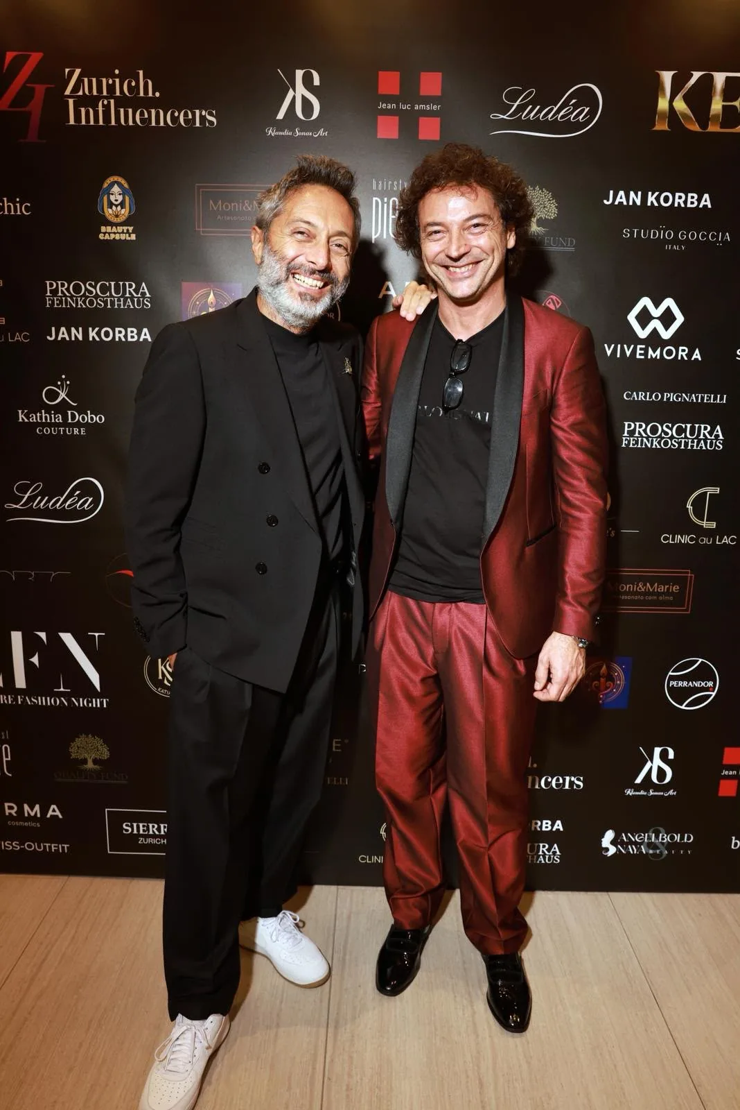 Two guests posing together at the Couture Fashion Night after-party against a branded step-and-repeat backdrop